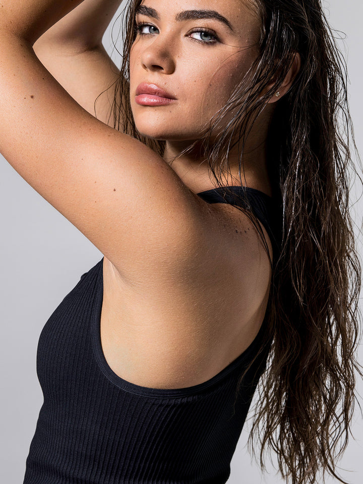 Close-up of woman wearing black Ribbed Racer Back Tank, posing with wet hair and arms raised.