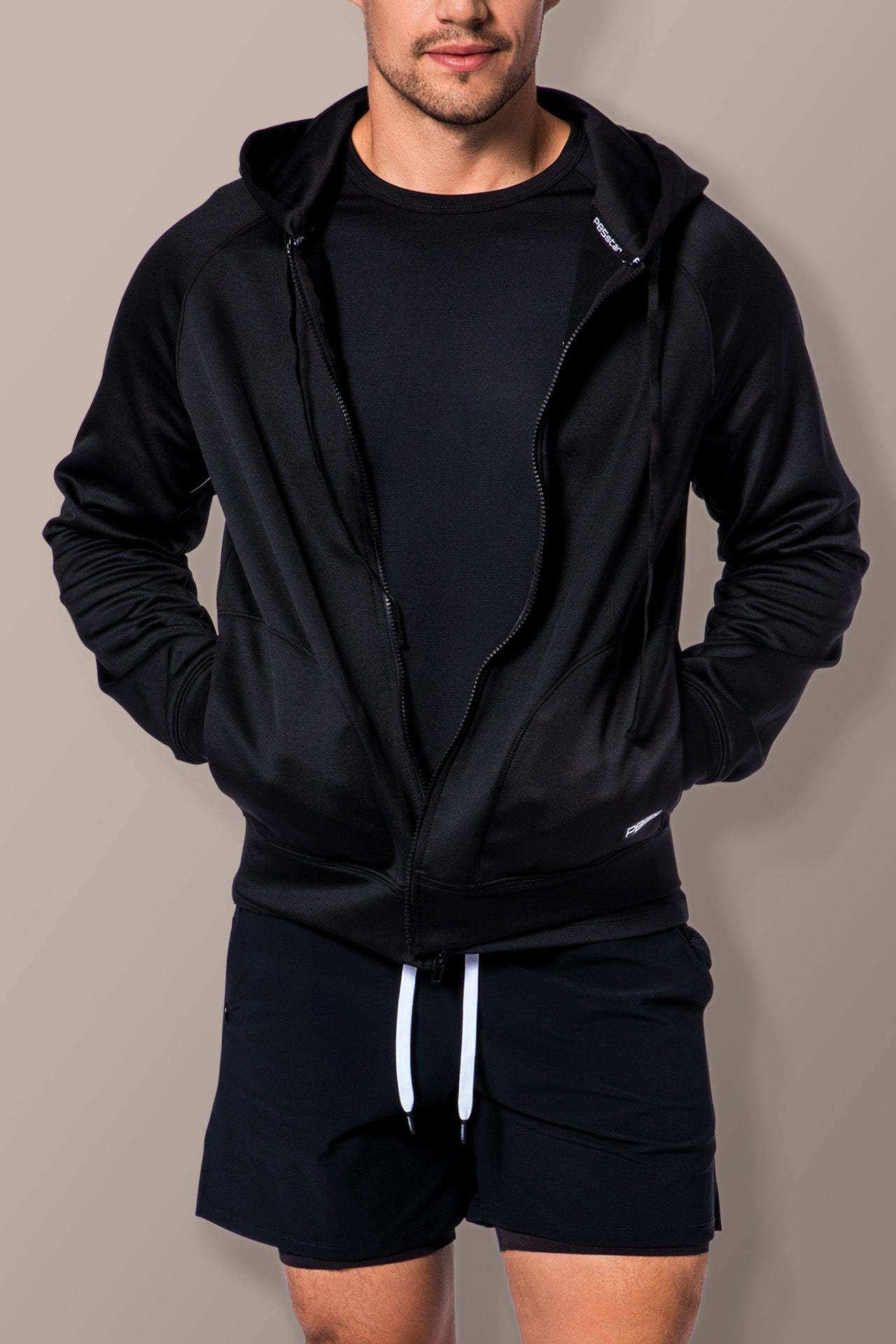 Close up of male model wearing PB5star black signature court shorts paired with performance full-zip hoodie.