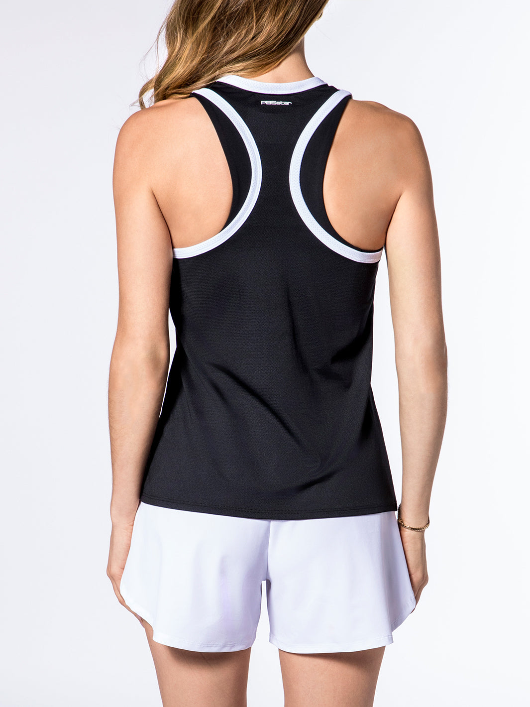 Rear view of a woman wearing PB5star's Core Tank in black with white trim, paired with white Signature Court Shorts, showcasing a sleek design that's both fashionable and functional for pickleball sportswear