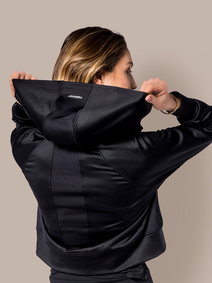 Woman pulling on the hood of a PB5Star black Cropped Performance Hoodie, displaying the stretchable fabric and fit.