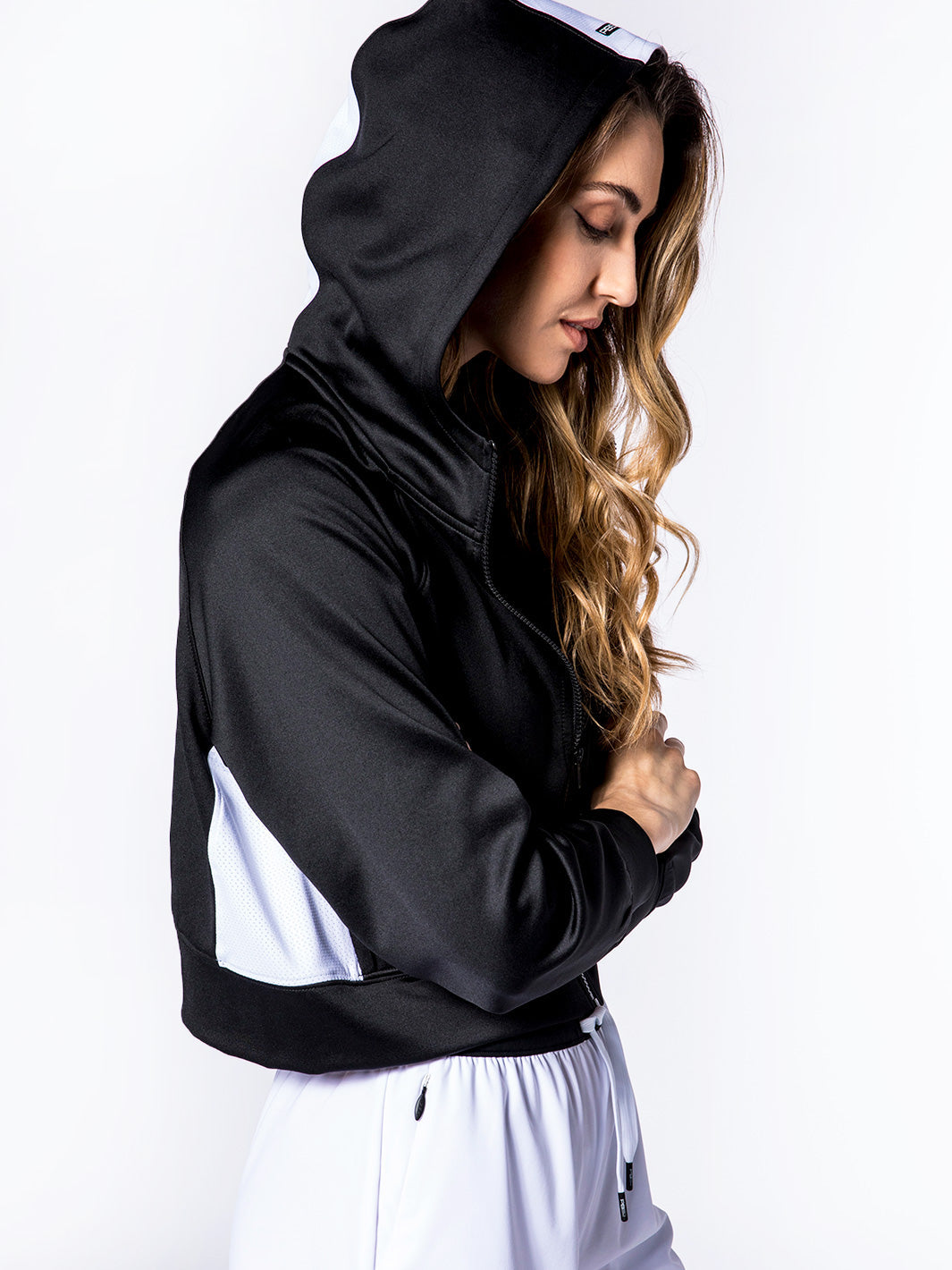 Side view of model wearing cropped hoodie in black and white. Hoodie is black with white panels on sides and white strip down back.