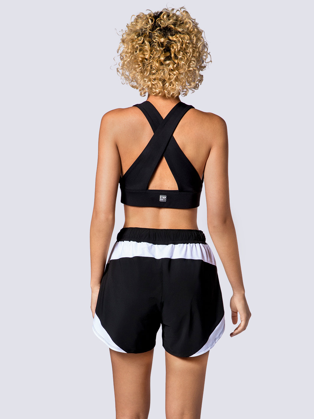 Rear view of a PB5star Vented Court Short in black and white, paired with a black sports bra for a sleek workout ensemble.